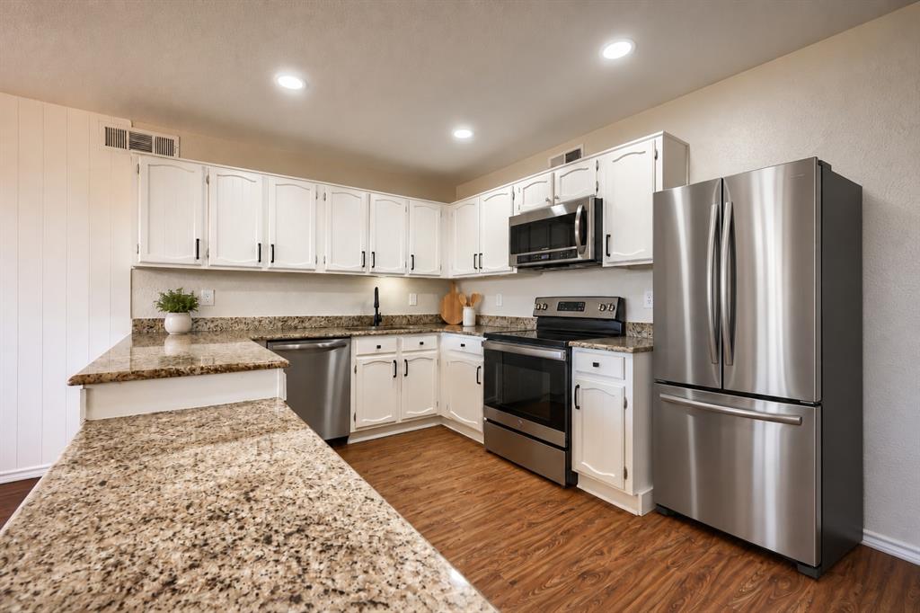 Kitchen featuring white cabinetry, stone-finish countertops, stainless steel appliances, recessed lighting, and wood-finish flooring Kitchen featuring white cabinetry, stone-finish countertops, stainless steel appliances, recessed lighting, and wood-finish flooring