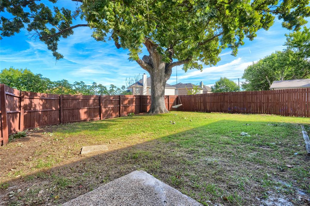 Spacious backyard featuring a wood privacy fence, a mature shade tree, and a concrete patio