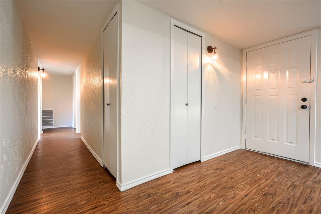 Wood-finish flooring, white paneled entry door with deadbolt, dual bi-fold closets, and wall-mounted sconce lighting