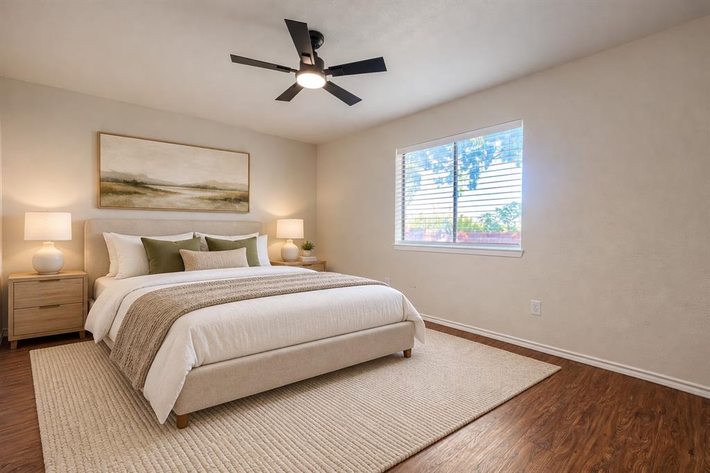 Wood-finish flooring, neutral wall tones, large window with horizontal blinds, and a central ceiling fan with integrated lighting