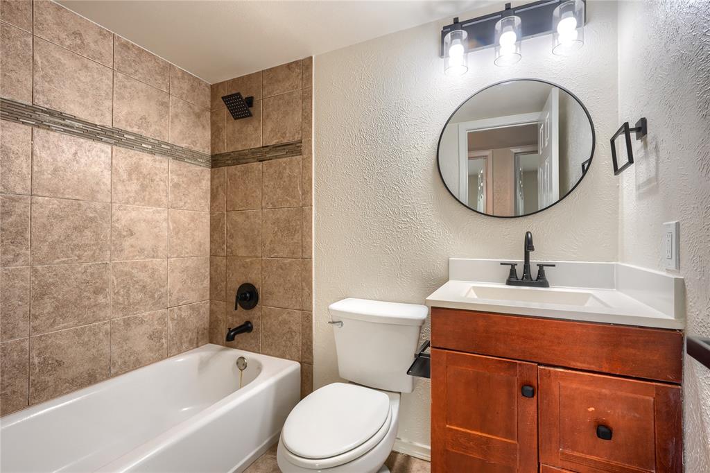 Bathroom featuring a wood-finish vanity with a white countertop, oval wall-mounted mirror, matte black plumbing fixtures, and a shower-tub combination with tile surround