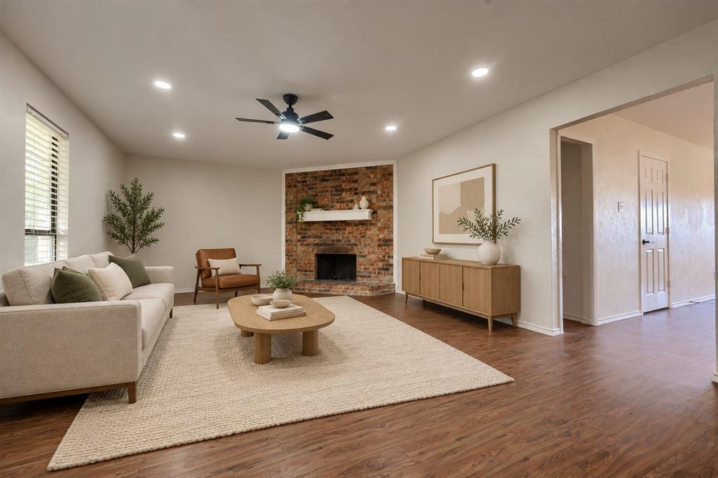 Living room featuring wood-finish flooring, a corner brick fireplace with a mantle, recessed ceiling lighting, and a ceiling fan