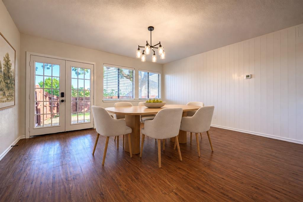 Dining area featuring wood-finish flooring, vertical shiplap wall detailing, multi-light chandelier, and double French doors with glass panes