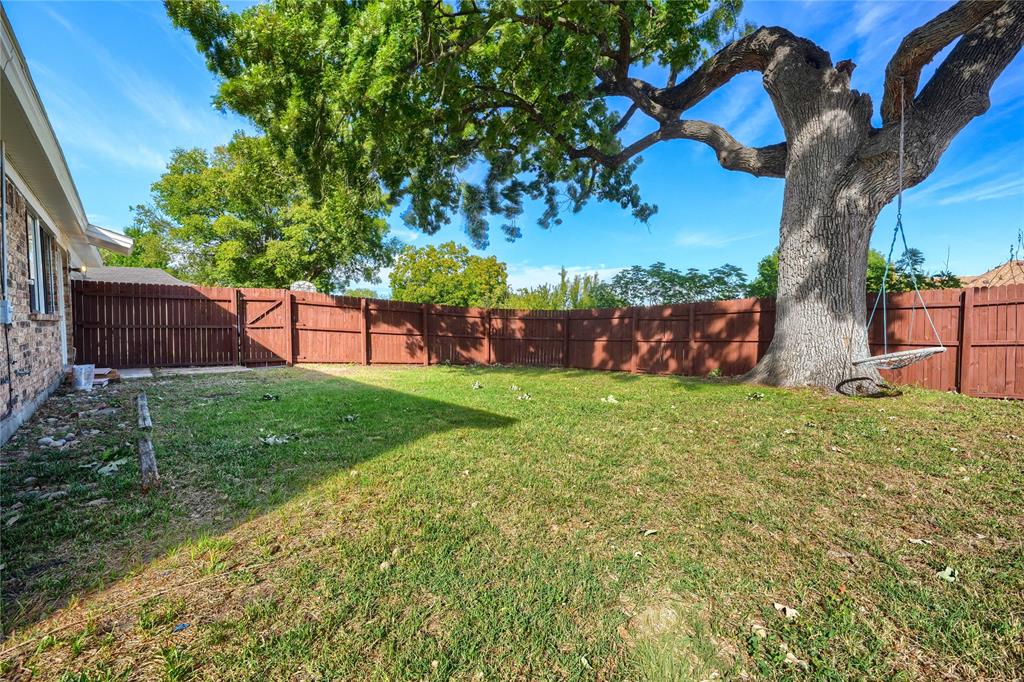 Expansive backyard featuring a mature canopy tree, privacy wood fencing, and a grass lawn