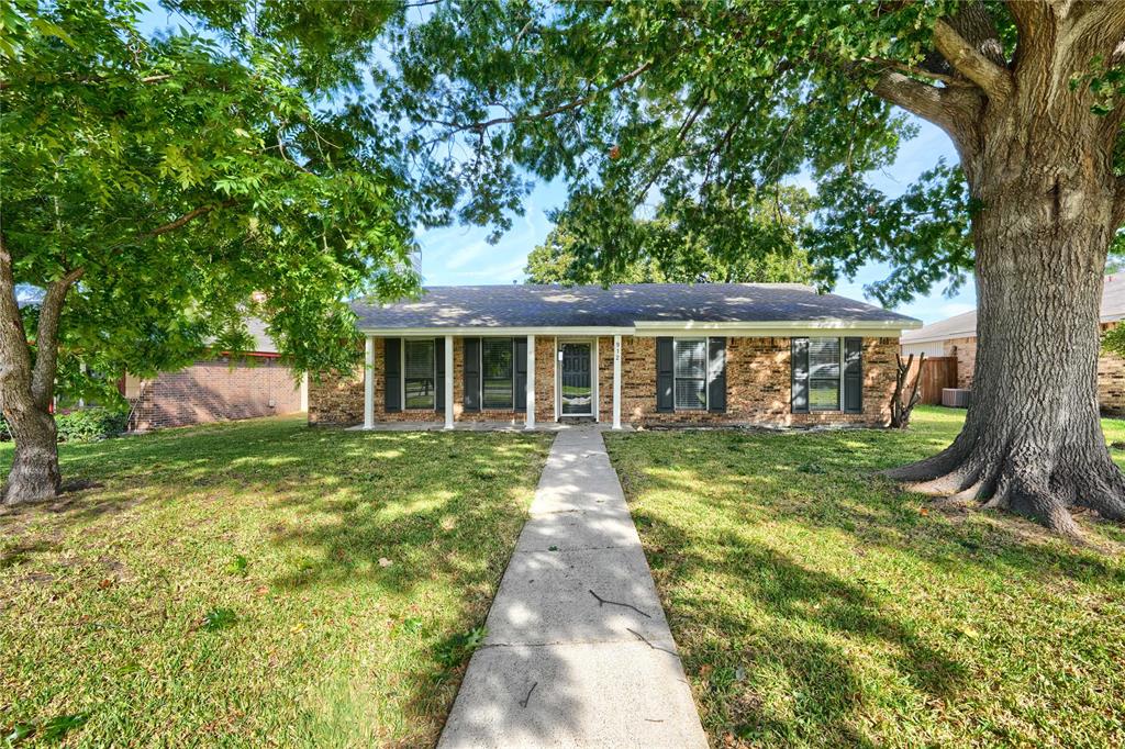 Single-story brick exterior featuring a covered front porch, decorative shutters, and mature trees situated on a grass-covered lot