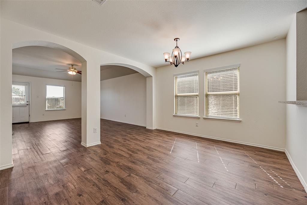 Wood-finish flooring, architectural arched openings, decorative multi-light chandelier, and dual windows with horizontal blinds