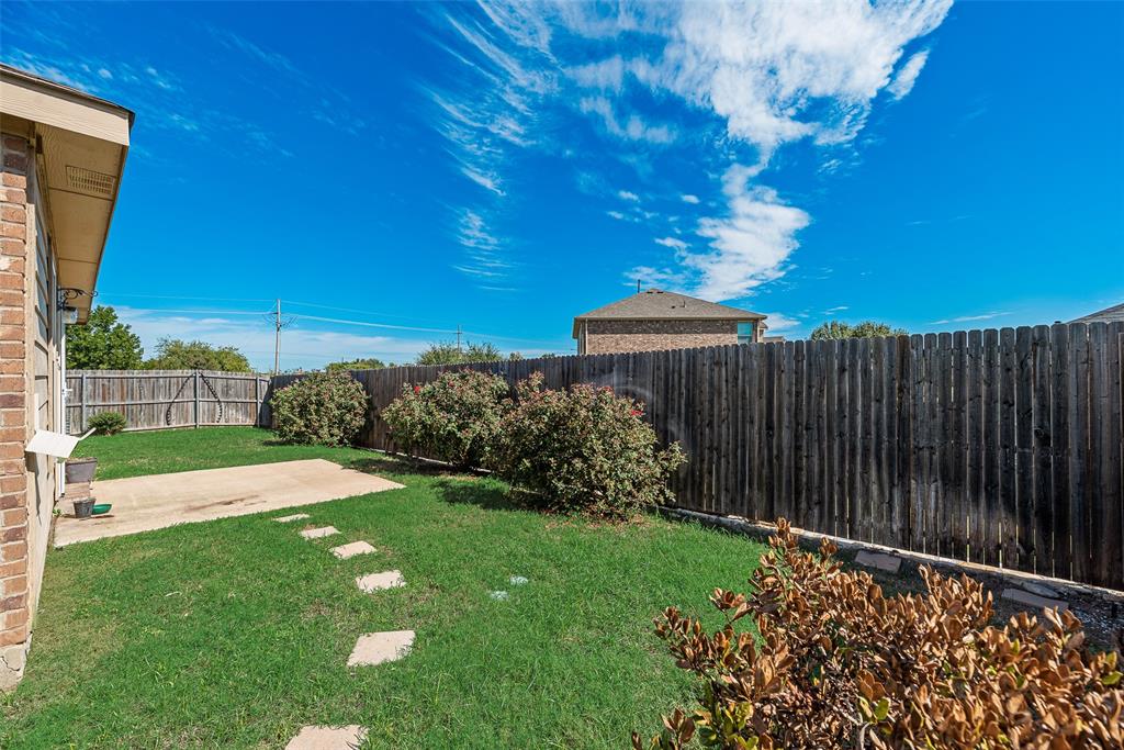 Fenced backyard featuring a concrete patio, stone paver pathway, lawn, and mature shrubs