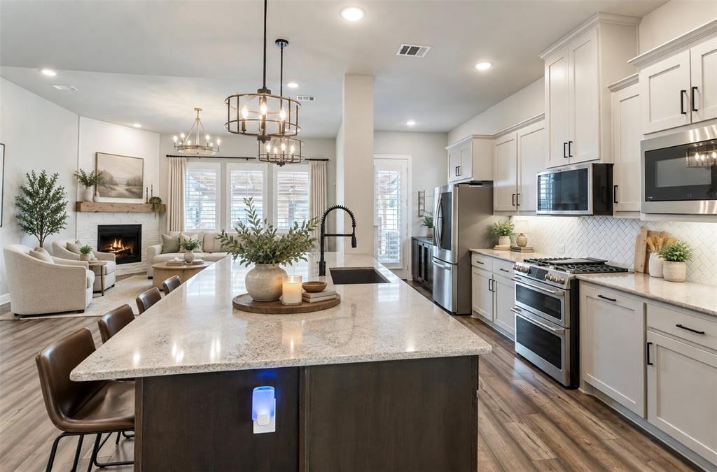 Kitchen featuring an expansive stone-topped island with an undermount sink, white shaker-style cabinetry, a herringbone-patterned tile backsplash, stainless steel appliances, and wood-finish flooring