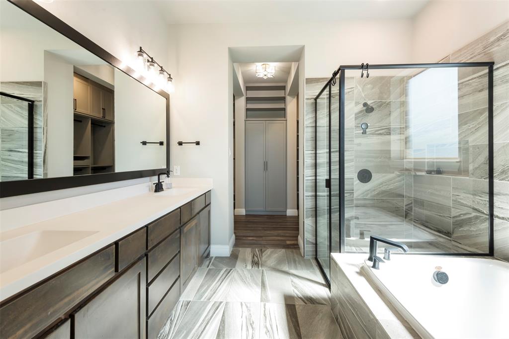 Double vanity with solid-surface countertops, large framed mirror, glass-enclosed shower with tiled surround, built-in cabinetry, and tile flooring