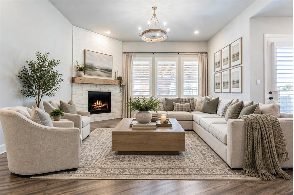 Corner fireplace with a textured brick surround and natural wood mantel, triple-pane window configuration with integrated shutters, wood-finish flooring, and a circular wagon wheel chandelier