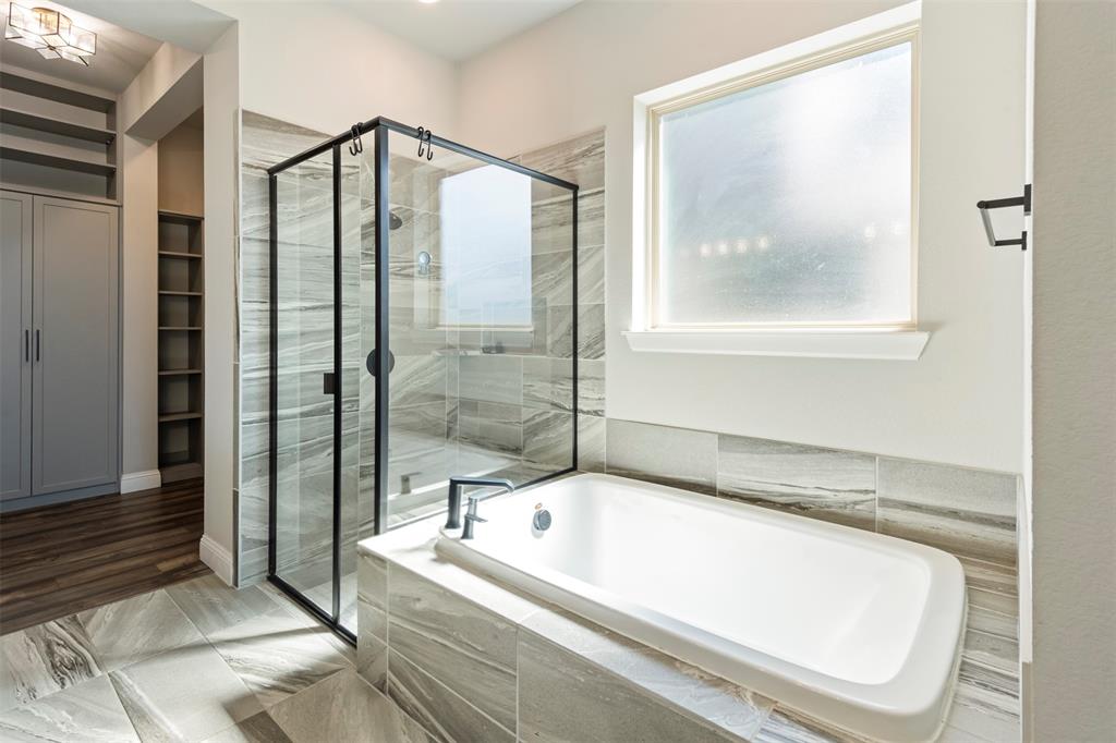 Bathroom featuring a soaking tub, glass-enclosed shower with matte black fixtures, stone-finish tile surround, and floor-to-ceiling built-in cabinetry