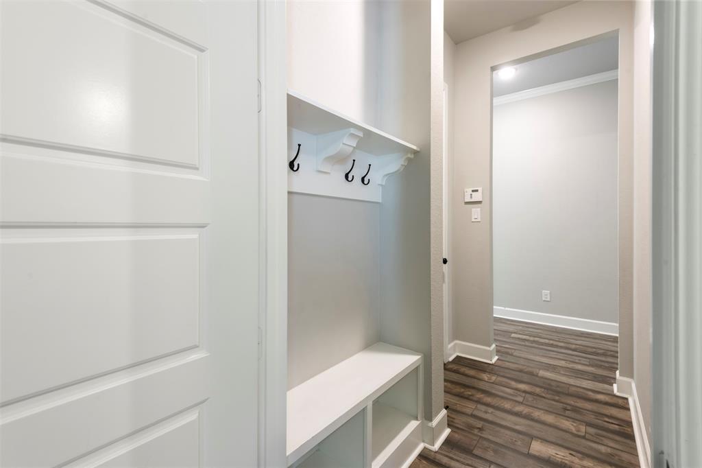 Built-in entryway storage featuring a bench, open shelving, and wall-mounted hooks, complemented by wood-finish flooring and a multi-panel door
