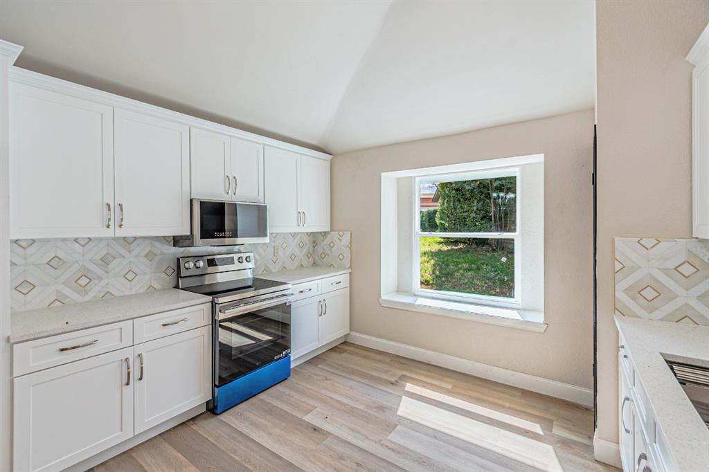 Kitchen featuring white cabinetry, light-toned stone-finish countertops, geometric patterned tile backsplash, stainless steel appliances, and wood-finish flooring