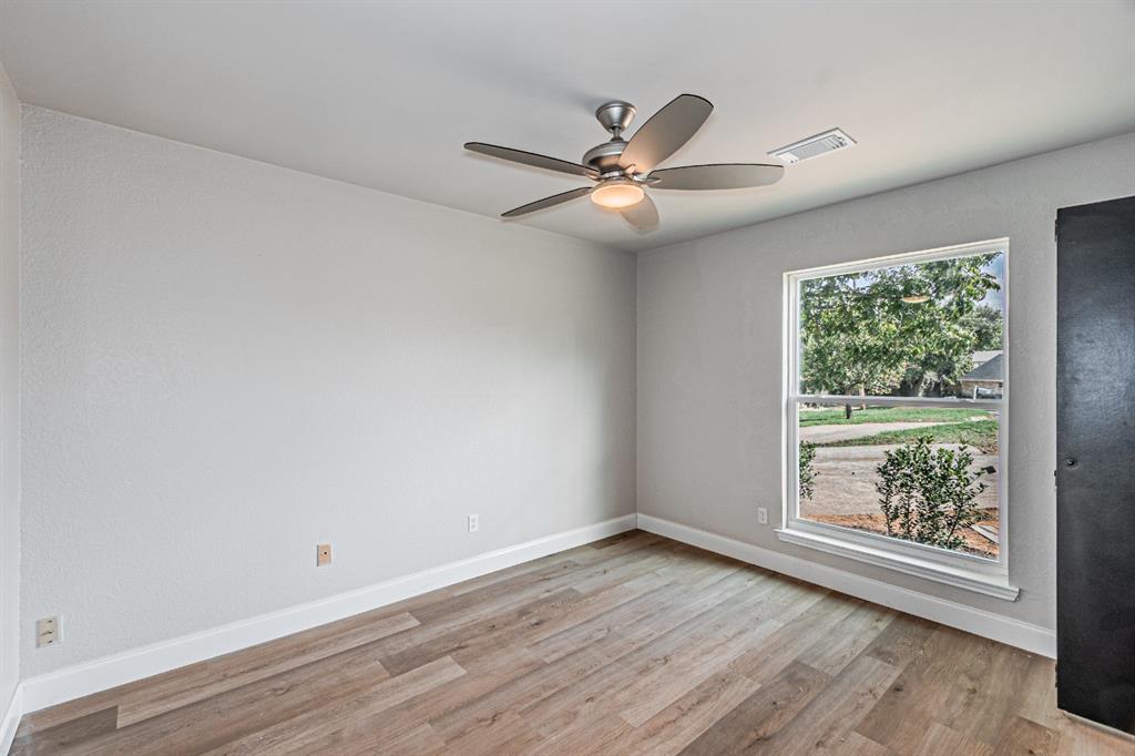 Neutral-toned interior space featuring wood-finish flooring, a ceiling fan with integrated lighting, and a window with exterior greenery