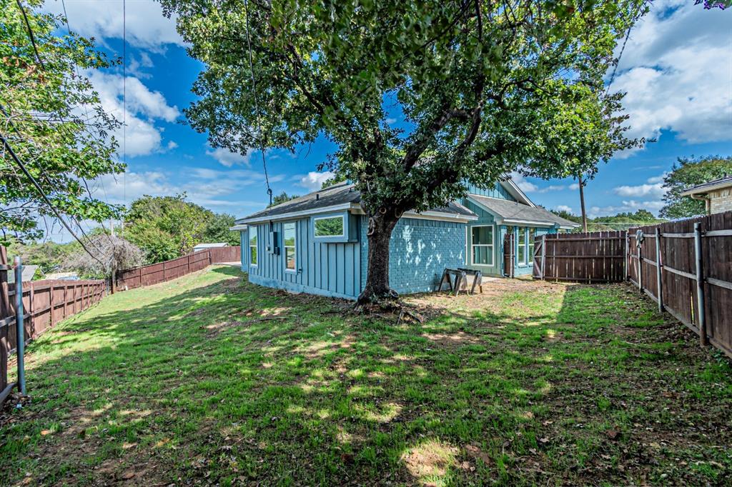 Rear yard featuring a mature shade tree, natural grass lawn, and perimeter wood privacy fencing