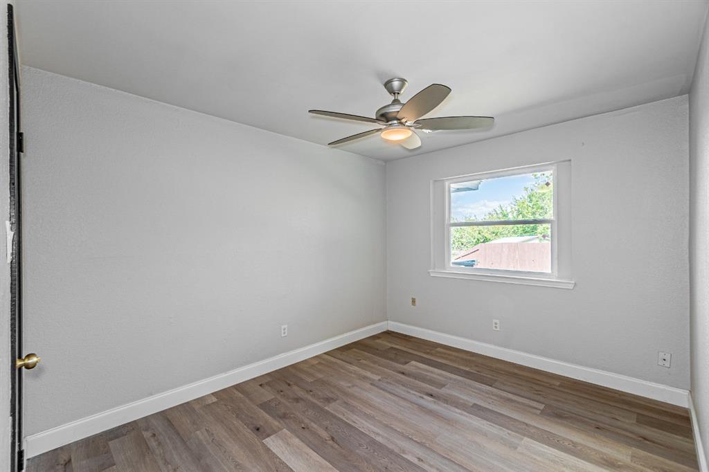Neutral-toned interior room featuring wood-finish flooring, a multi-blade ceiling fan with integrated lighting, and a single-pane window