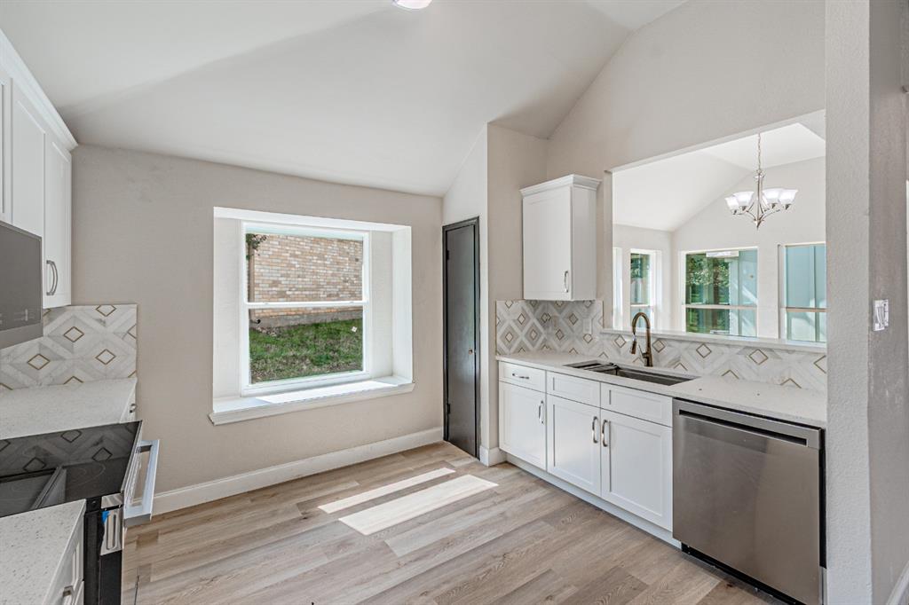 Kitchen featuring vaulted ceilings, light wood-finish flooring, quartz countertops, geometric patterned tile backsplash, and white cabinetry