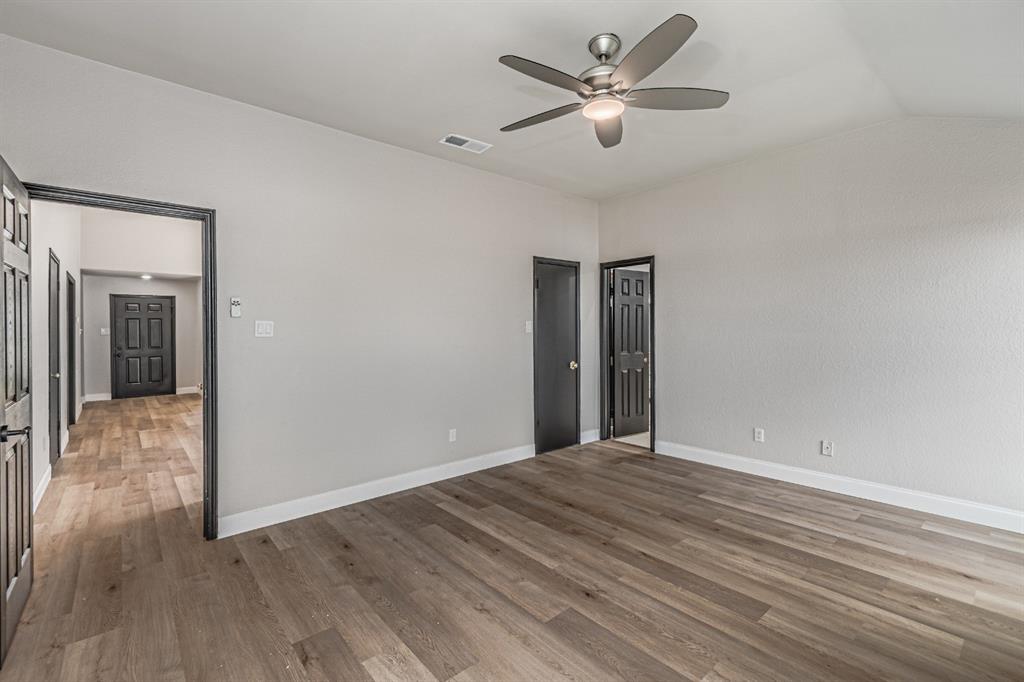 Vaulted ceiling featuring a central brushed-nickel ceiling fan with integrated lighting, complemented by wood-finish flooring and high-contrast dark door frames