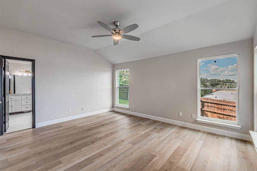 Vaulted ceiling featuring a central multi-blade ceiling fan, wood-finish flooring, and dual picture windows