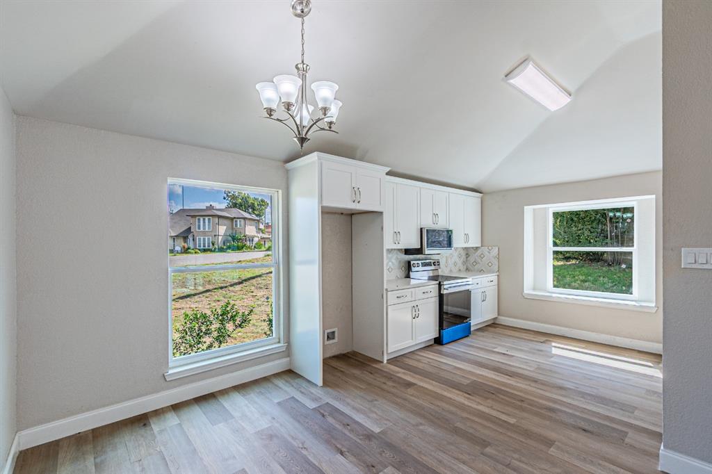 Vaulted ceilings, wood-finish flooring, white shaker-style cabinetry, patterned tile backsplash, and multi-light chandelier