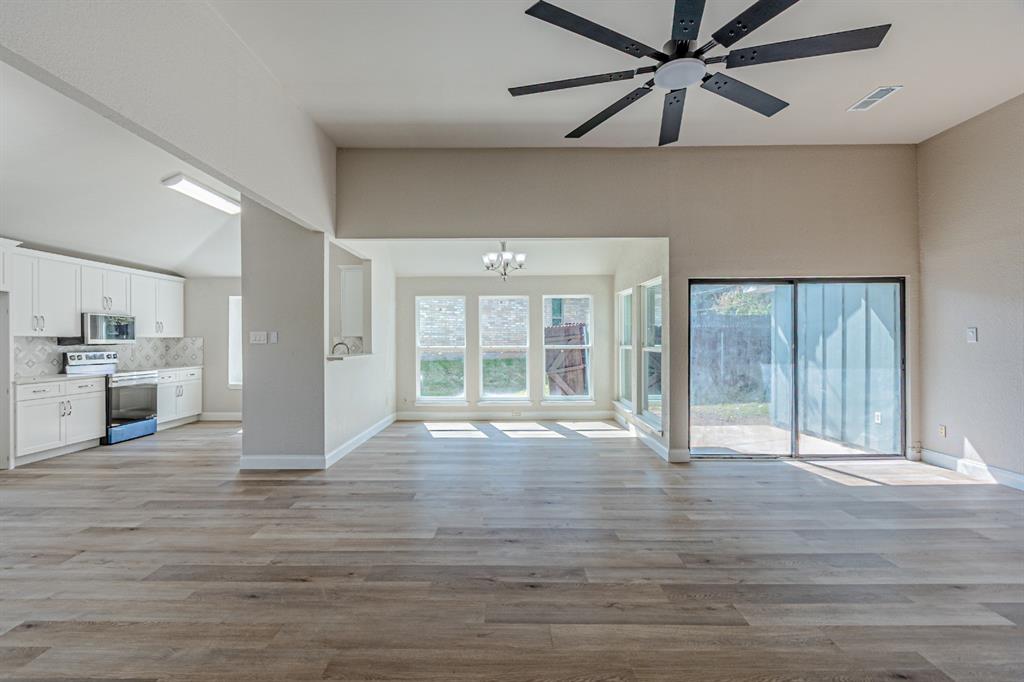 Open-concept interior featuring wood-finish flooring, vaulted ceilings, a multi-blade ceiling fan, white cabinetry, and sliding glass doors