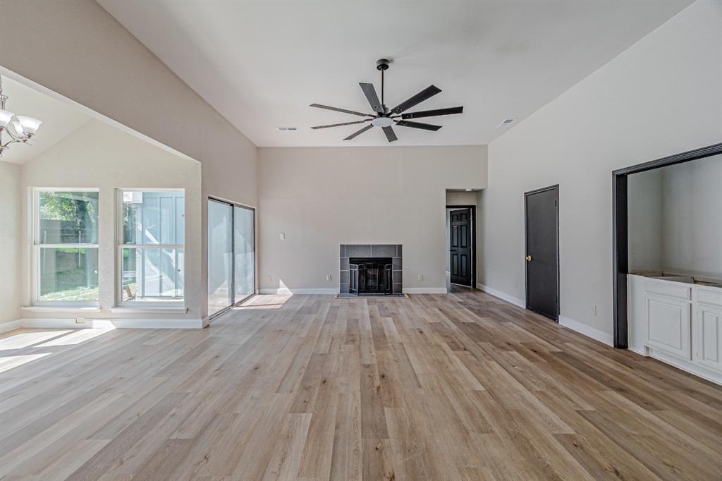 Living area featuring vaulted ceilings, wood-finish flooring, a fireplace with a stone-surround facade, a multi-blade ceiling fan, and built-in cabinetry