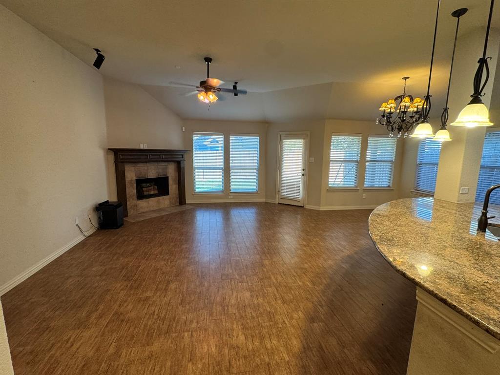 Open-concept space featuring wood-finish flooring, vaulted ceilings, a fireplace with stone-surround and timber mantle, stone-surface breakfast bar, and multiple pendant light fixtures