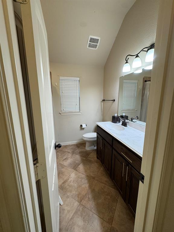 Dark wood-finish cabinetry featuring dual-basin vanity with a solid surface countertop, ceramic tile flooring, and vaulted ceiling