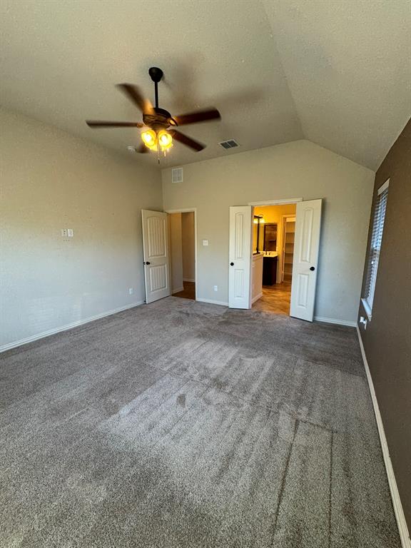 Vaulted ceilings featuring a central ceiling fan with integrated lighting, neutral wall tones, carpeted flooring, and double doors opening to an auxiliary space