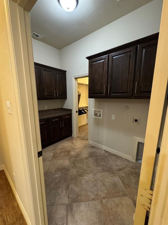 Utility room featuring dark-finish cabinetry, stone-texture countertops, tile flooring, and wall-mounted storage units