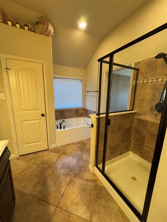 Soaking tub with tile surround, glass-enclosed shower with tiled walls, and large-format tile flooring