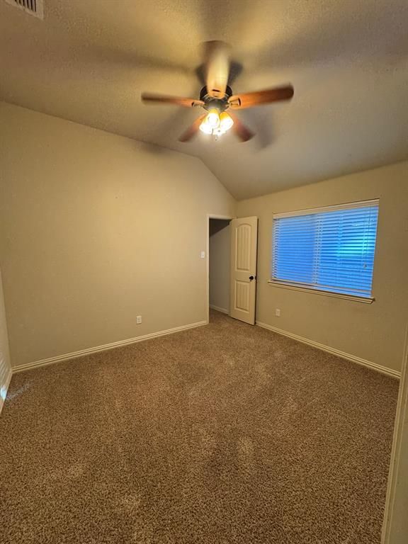 Vaulted ceiling with a centrally mounted ceiling fan featuring integrated tri-bulb lighting, neutral carpeting, and window with horizontal blinds