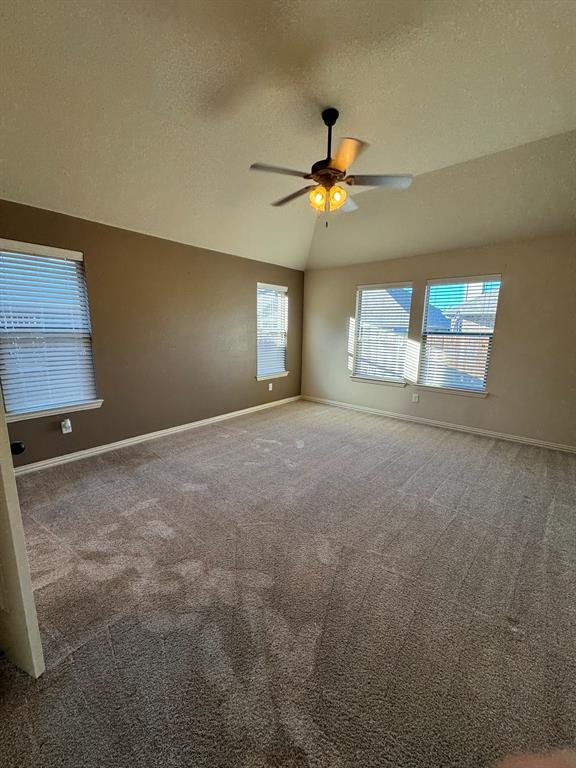Vaulted ceiling featuring a central multi-blade ceiling fan with integrated lighting, neutral wall tones, and carpeting