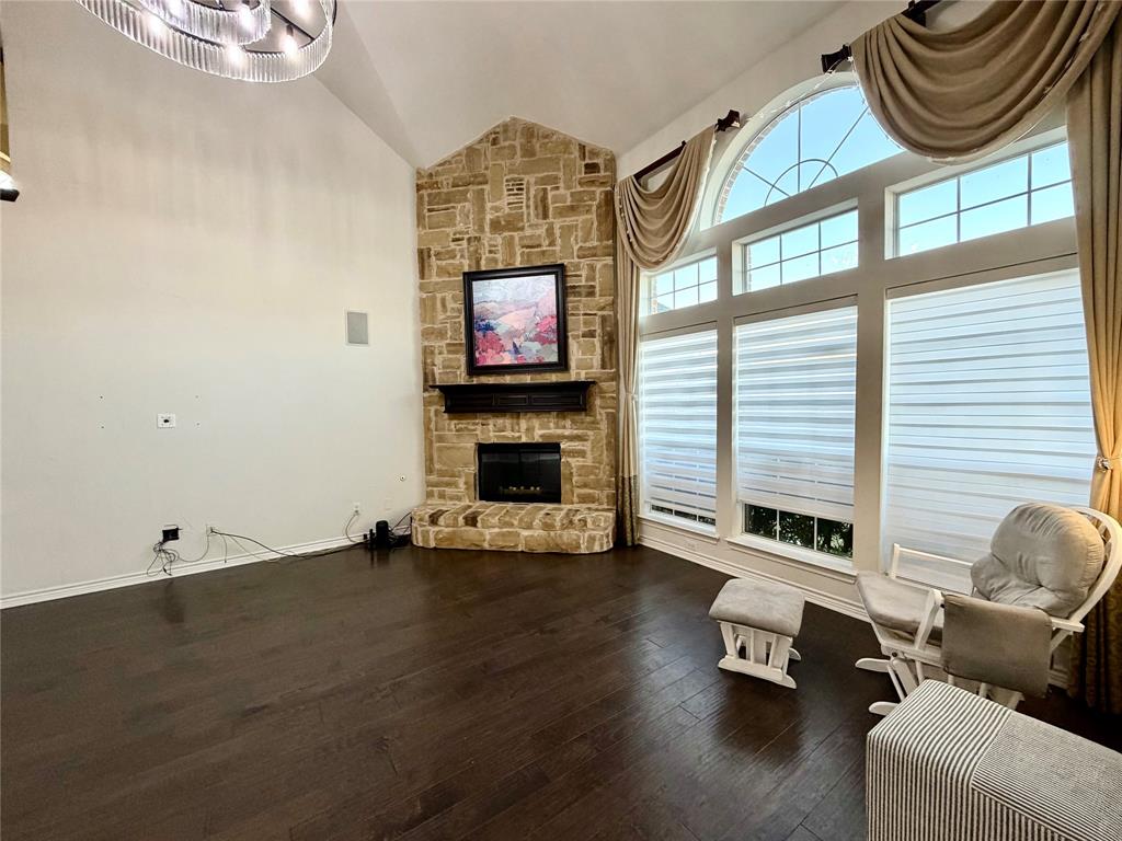 Vaulted ceilings, floor-to-ceiling stone fireplace with a dark wood mantel, wood-finish flooring, and a multi-pane arched window ensemble