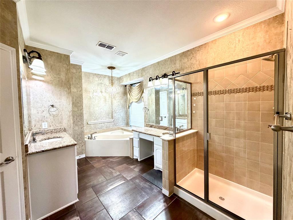Bathroom featuring tile flooring, a walk-in shower with glass enclosure, corner soaking tub, dual-sink vanity with stone countertop, and crown molding