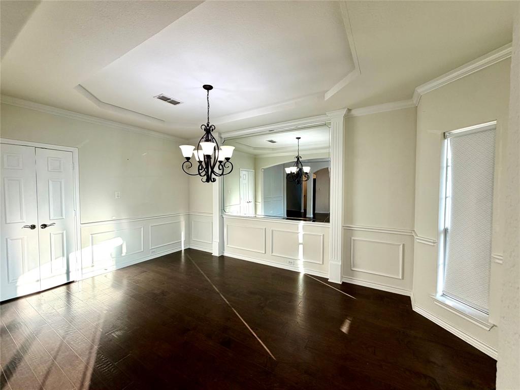 Dining area featuring dark wood-finish flooring, recessed tray ceiling, custom wainscoting, integrated wall mirror, and a multi-light decorative chandelier