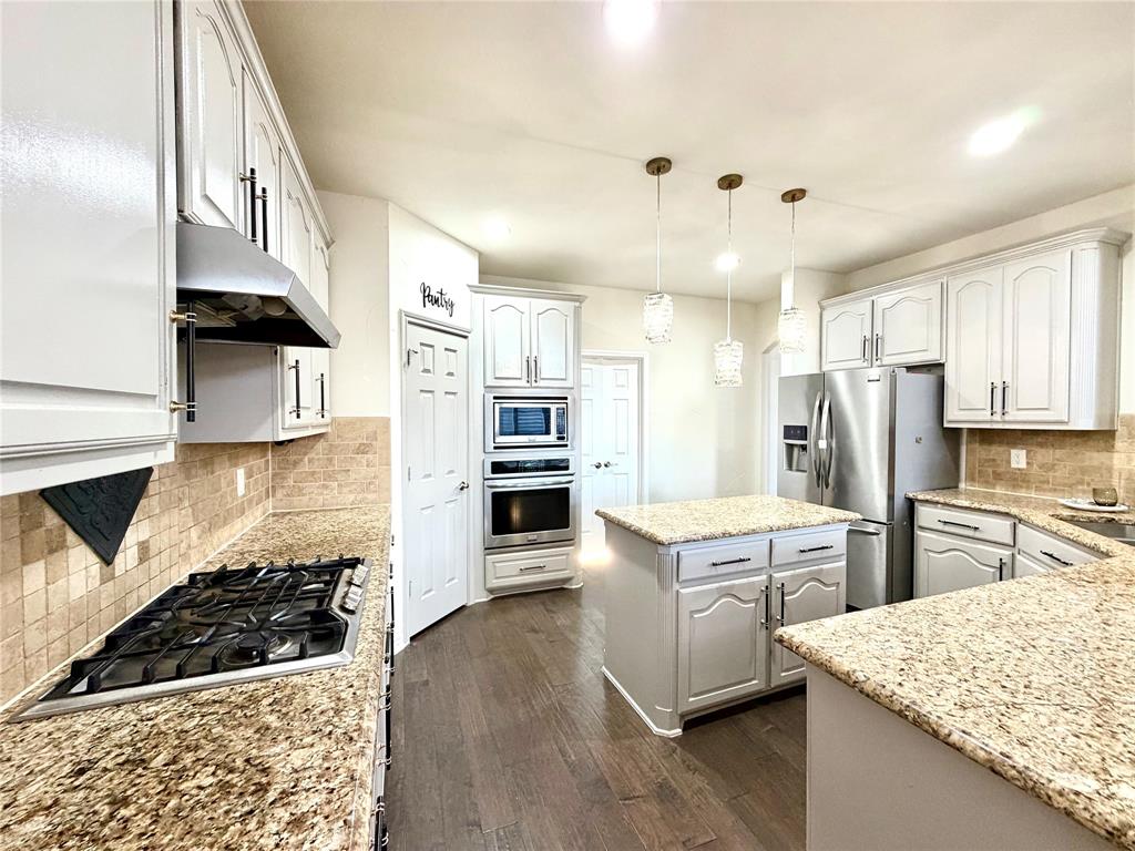 Kitchen featuring stone countertops, white cabinetry, wood-finish flooring, stainless steel built-in appliances, and pendant lighting
