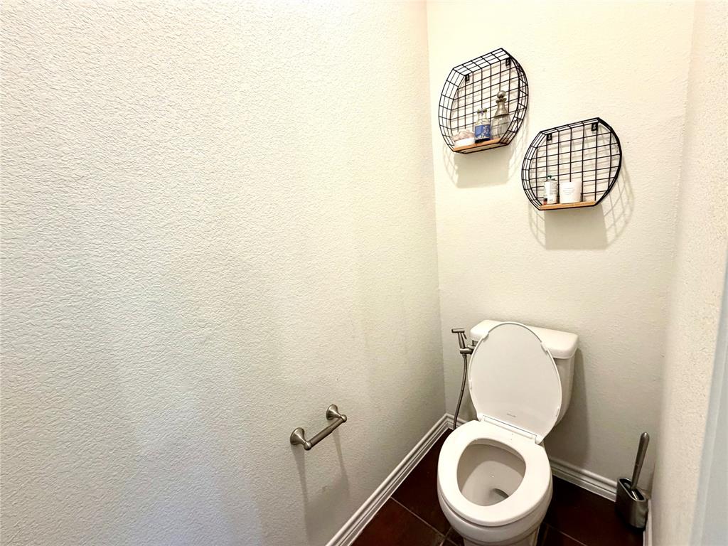 Restroom featuring dark ceramic tile flooring and a dual-flush toilet with an integrated bidet sprayer