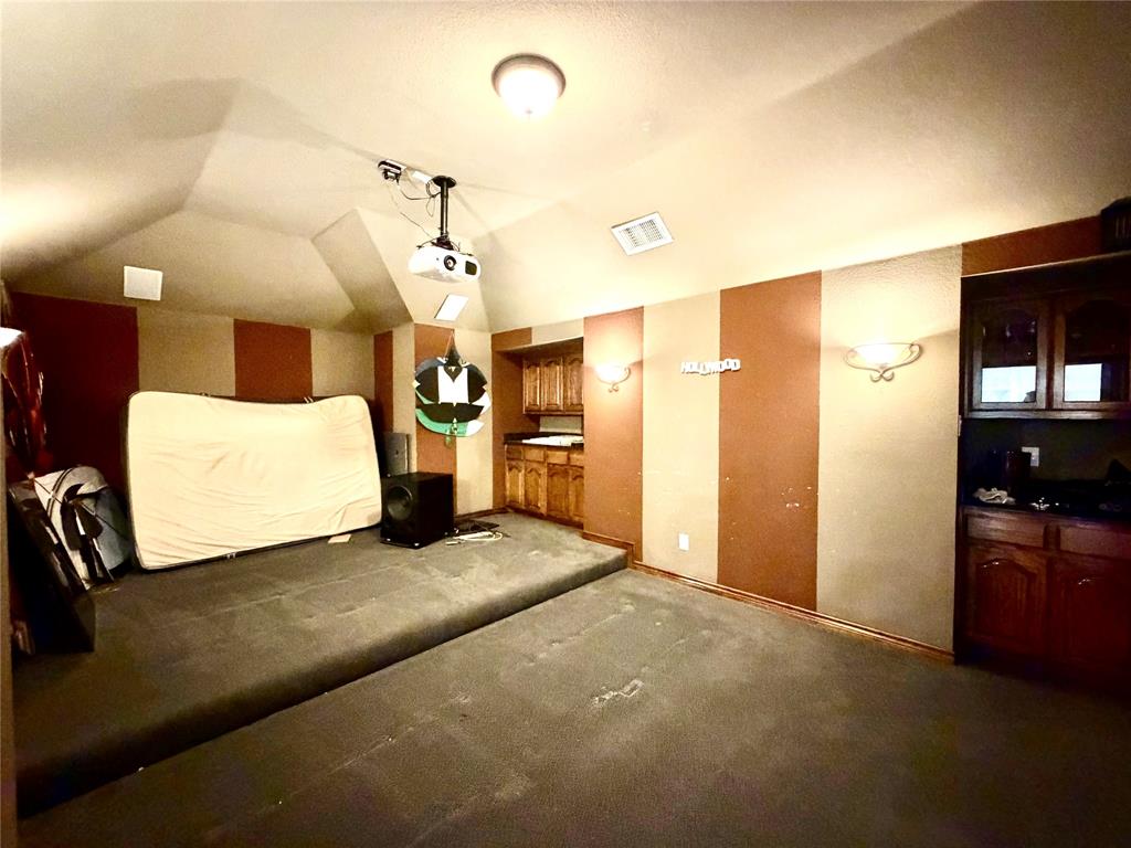 Vaulted ceilings with mounted projector, tiered carpeted flooring, and built-in wood cabinetry with stone countertops