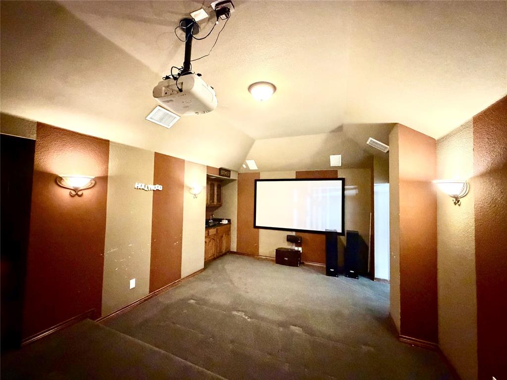 Media room featuring tiered flooring, a ceiling-mounted projector, wall-mounted light fixtures, and built-in cabinetry with a countertop
