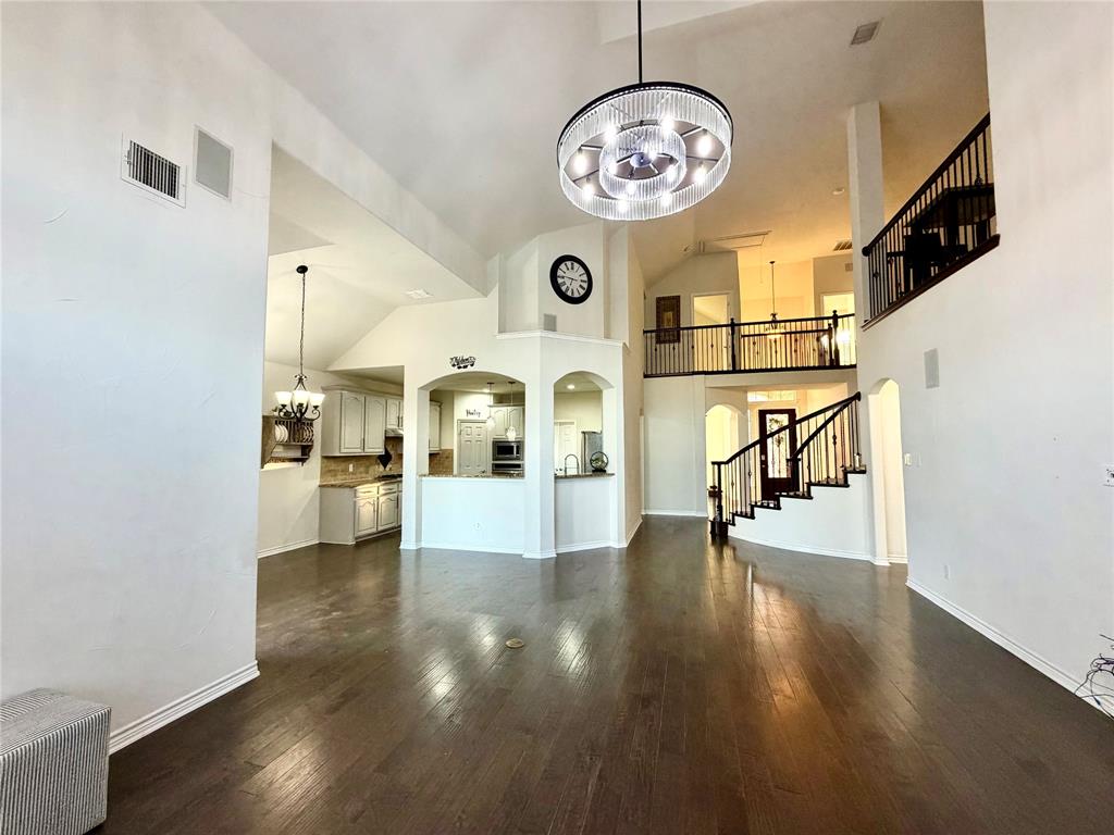Double-height ceiling with a modern drum chandelier, dark wood-finish flooring, staircase with a black metal balustrade, and arched architectural wall detailing