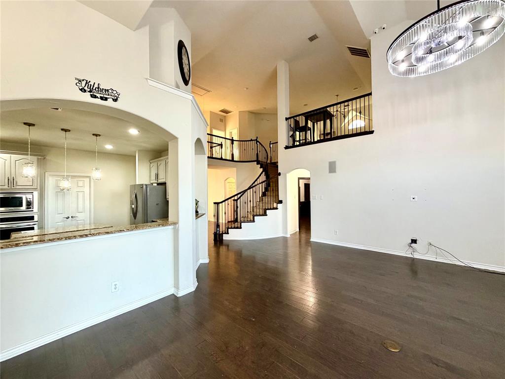 Interior featuring high ceilings, wood-finish flooring, a curved staircase with wrought-iron railings, a mezzanine landing, and a contemporary oval-shaped pendant light fixture