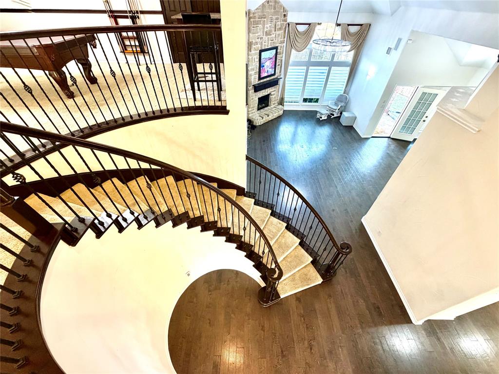 Curved staircase featuring wood handrails and metal balusters, soaring vaulted ceilings, stone-clad fireplace, wood-finish flooring, and multi-pane windows