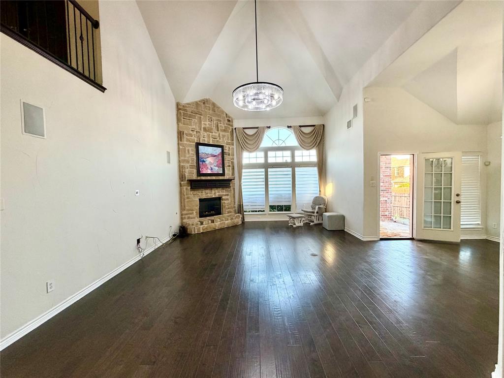 Vaulted ceiling featuring a stone-clad fireplace, dark wood-finish flooring, large multi-pane windows, and a suspended circular chandelier