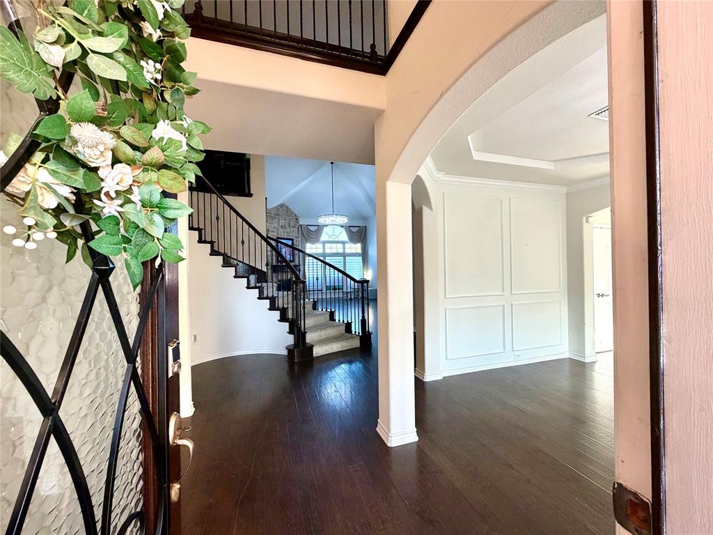 Foyer entrance featuring wood-finish flooring, a two-story ceiling, a wrought-iron staircase railing, arched wall detailing, and a tray ceiling