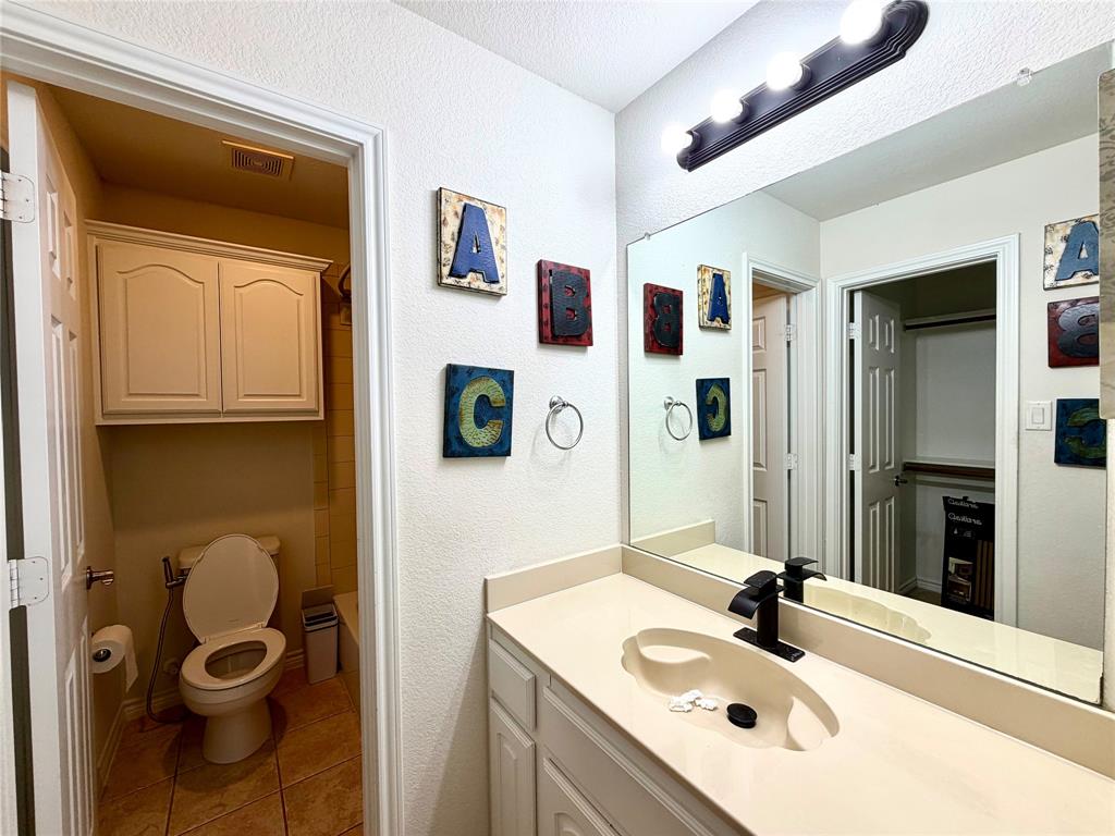 Vanity featuring a solid surface countertop with an integrated basin, matte black faucet, full-width mirror, wall-mounted light fixture, and white cabinetry