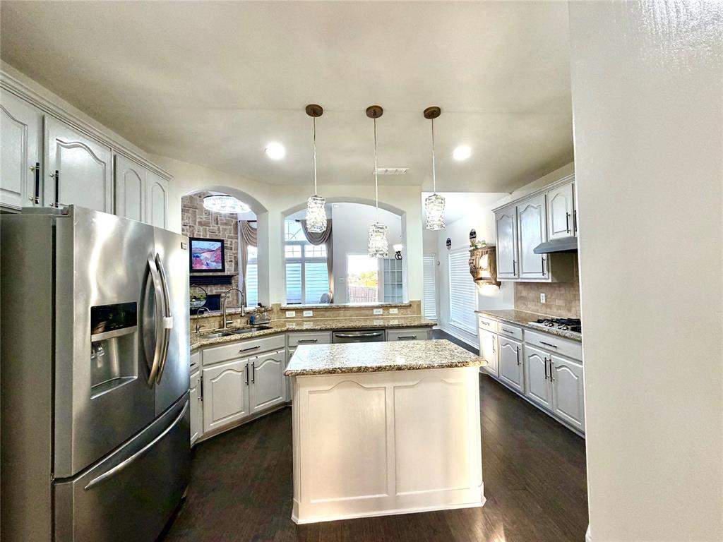 Kitchen featuring a central island with a stone-finish countertop, white cabinetry with matching hardware, stainless steel refrigerator, recessed lighting, and three glass pendant fixtures