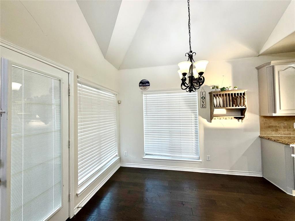 Vaulted ceiling, dark wood-finish flooring, multi-light iron chandelier, built-in wooden wall shelving, and a full-lite glass door