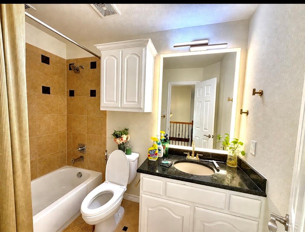 Bathroom featuring a vanity with dark stone countertop, undermount sink, and brass-tone hardware, paired with a wall-mounted medicine cabinet, backlit mirror, and a tile-surround tub