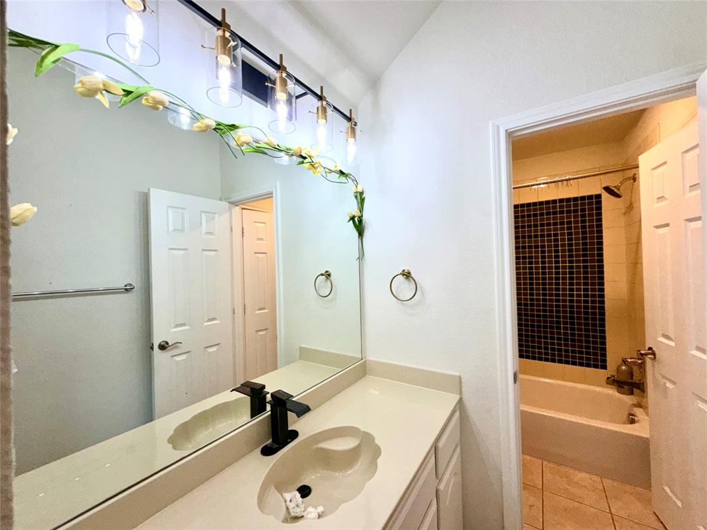 Bathroom featuring an integrated vanity countertop with an oval basin, matte black faucet, four-light glass vanity fixture, and a tiled shower surround